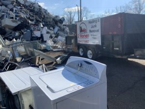 A washing machine and other metal junk with a 2 Women with a Pickup Truck and Trailer Too LLC trailer in the background, ready for removal in Columbus, OH.