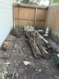 A backyard corner with old logs, bricks, and various debris, ready for removal by Handymen Junk Removal in Houston, TX.