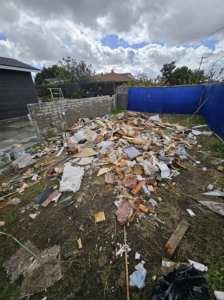 A backyard filled with a large pile of mixed construction debris and trash, ready for removal by Dos Muchos Junk Removal LLC in San Diego, CA.