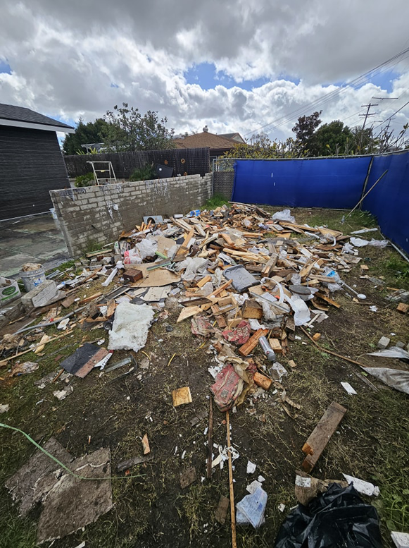 A backyard filled with a large pile of mixed construction debris and trash, ready for removal by Dos Muchos Junk Removal LLC in San Diego, CA.