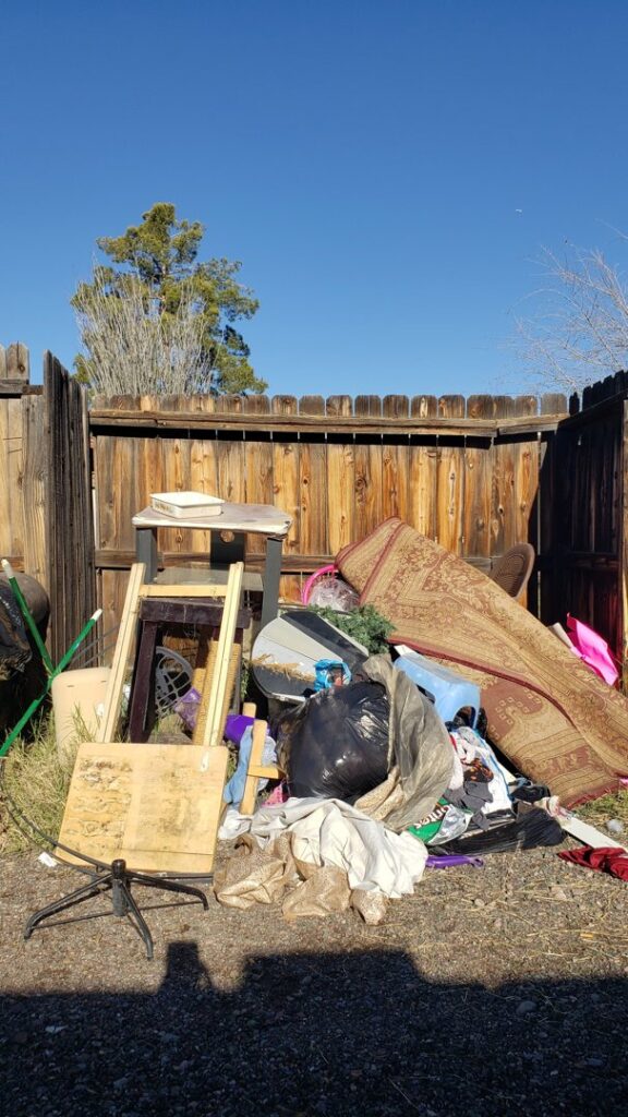 A backyard pile of miscellaneous junk, including an old rug and furniture parts, ready for J & R Junk Removal in Phoenix, AZ.