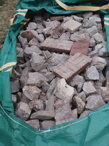 A large green bag filled with concrete and brick debris, ready for removal by Lolo Hauling Junk Removal in Dallas, TX.