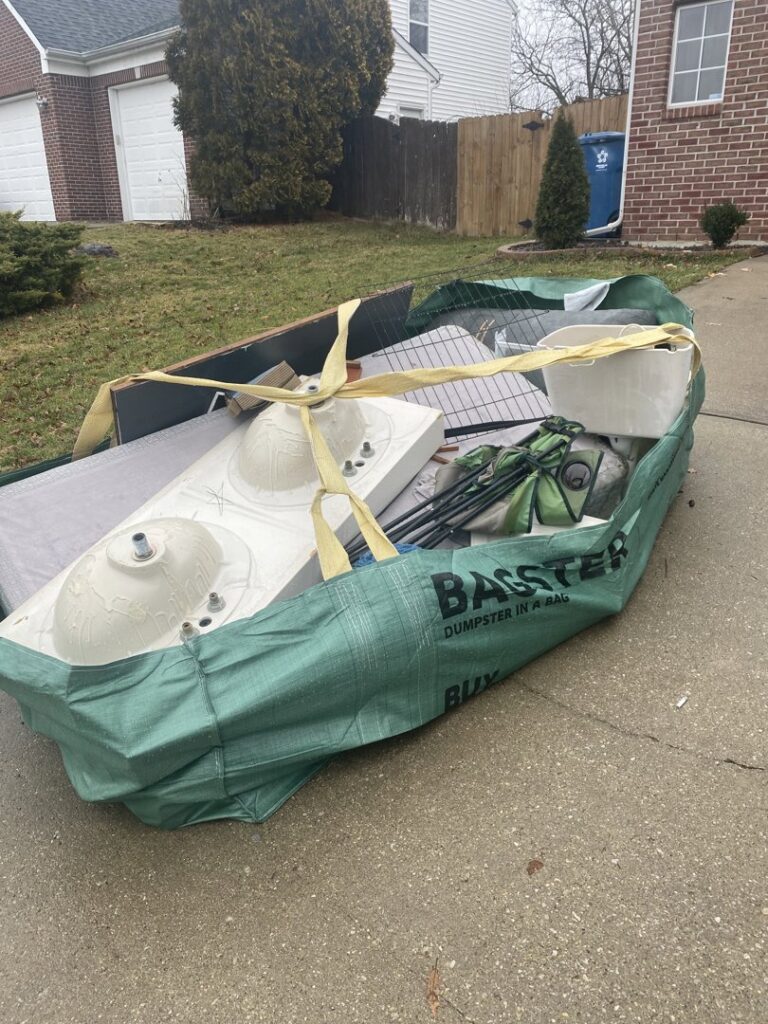 A large Bagster-style bag filled with sinks, a mattress, and other debris on a driveway, ready for pickup by ABC Junk Removal & Hauling in Westfield, IN.