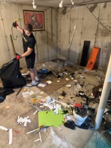 A Junk to Go worker performing a basement cleanout, collecting debris into a trash bag in Philadelphia, PA.