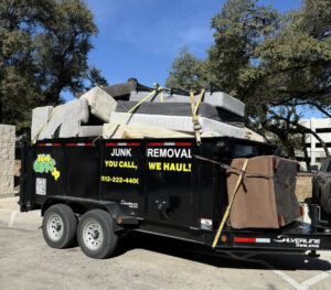 A black JunkGuys Austin Junk Removal trailer is fully loaded with old furniture and mattresses, securely strapped for transport in Austin, TX.