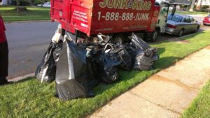 Numerous black trash bags filled with debris on a residential lawn next to a Junk King truck in Austin, TX