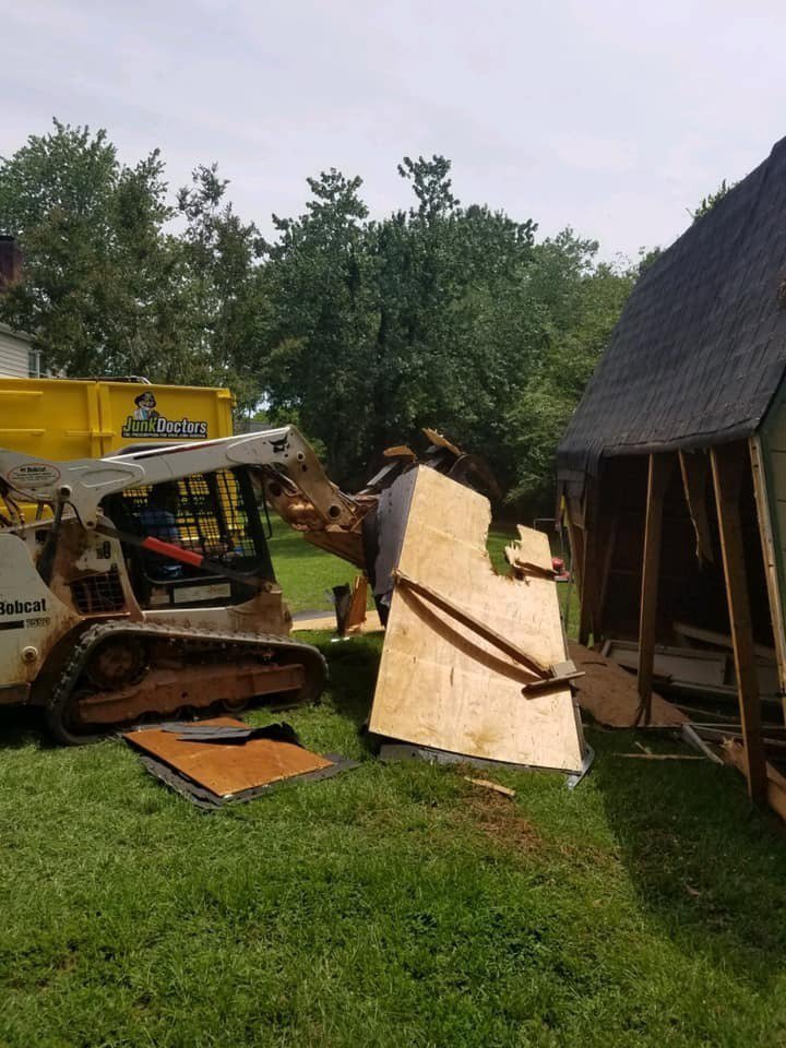 A Bobcat skid-steer loader clearing demolition debris towards a Junk Doctors of Charlotte truck in Charlotte, NC.