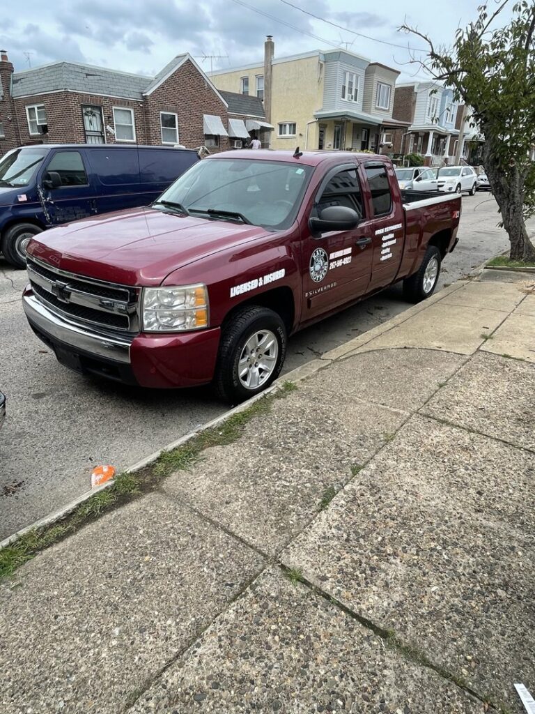 A branded red pickup truck from Kay's Brothers Junk Removal parked on a residential street in Philadelphia, PA.