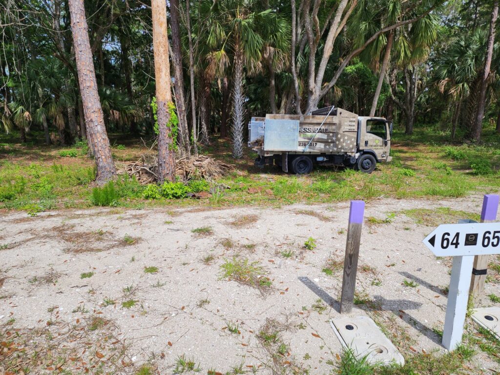 A junk removal truck from The Mess Haul parked near a large pile of brush and debris for removal in Jacksonville, FL.
