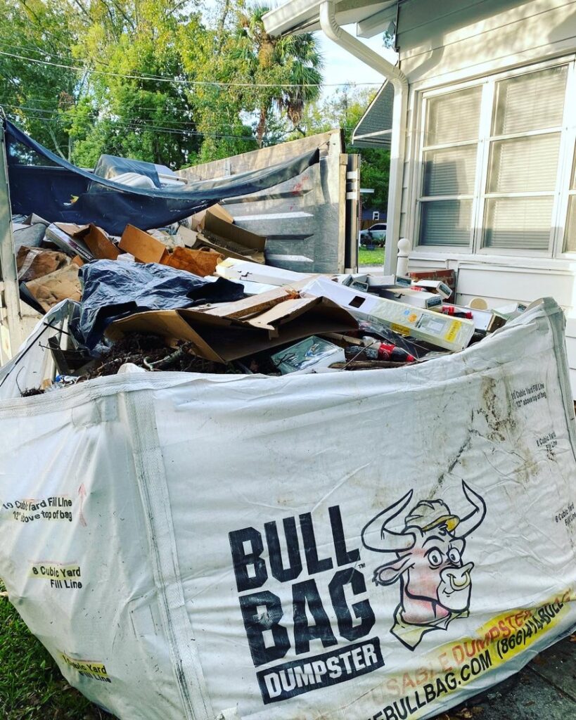 A large Bull Bag dumpster filled with various household and construction junk, demonstrating a debris removal service by Jacksonville Hauling & Junk Removal in Jacksonville, FL.