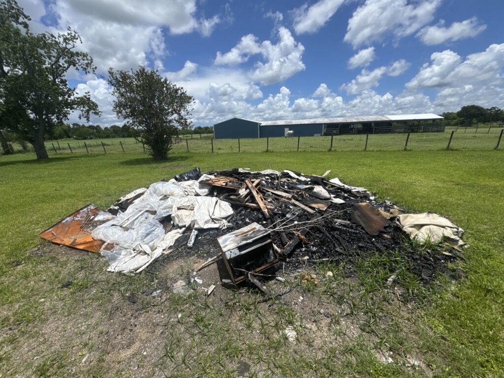 A large pile of burnt debris and trash in a field, requiring cleanup by Clear Your Junk - Pearland in Houston, TX.