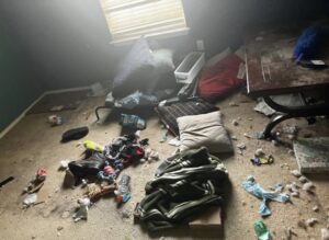 A cluttered bedroom floor covered with clothes, pillows, and debris, indicating a cleanout job for Junkie 4 Jesus Junk Removal in Austin, TX