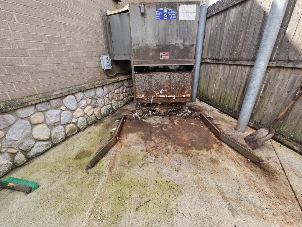 A commercial dumpster area with trash and debris on the ground, indicating a cleanup job by Purefoy's Professionals in Columbus, OH.