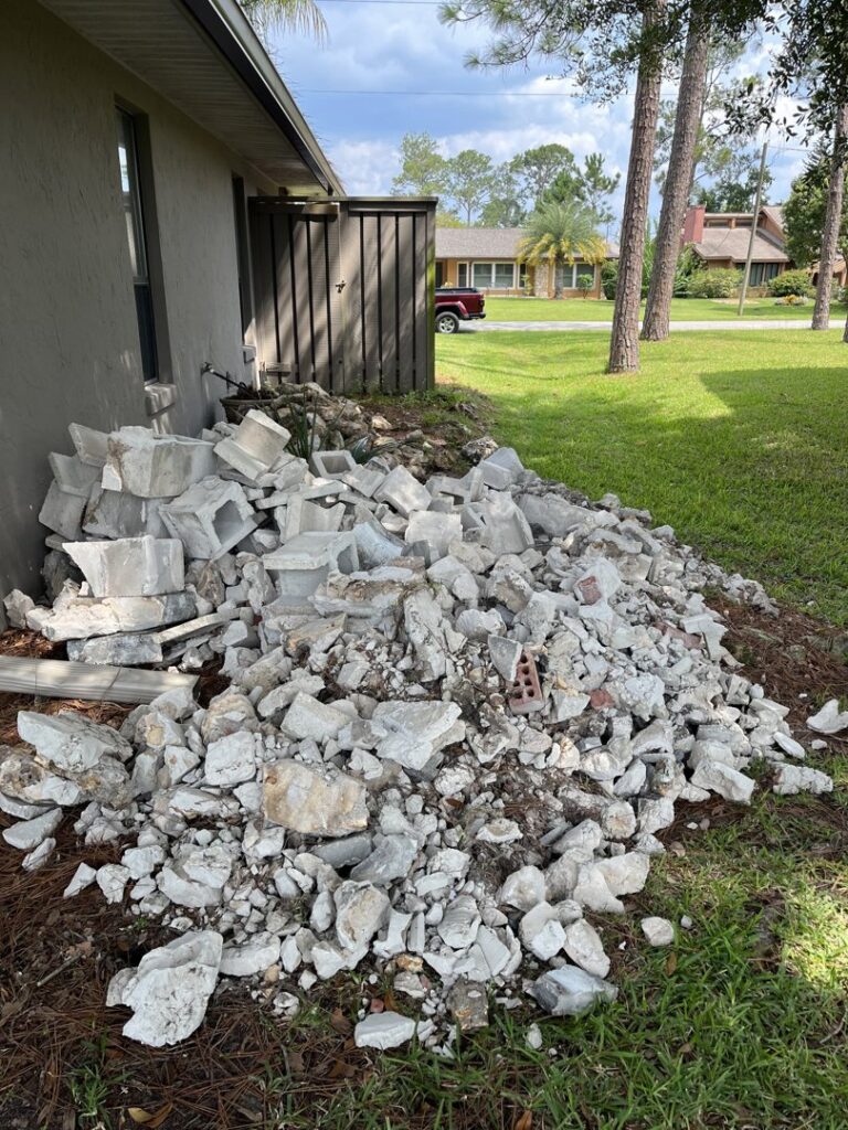 A large pile of broken concrete and masonry debris next to a residential building for removal by DUMP 4 U Hauling in Jacksonville, FL
