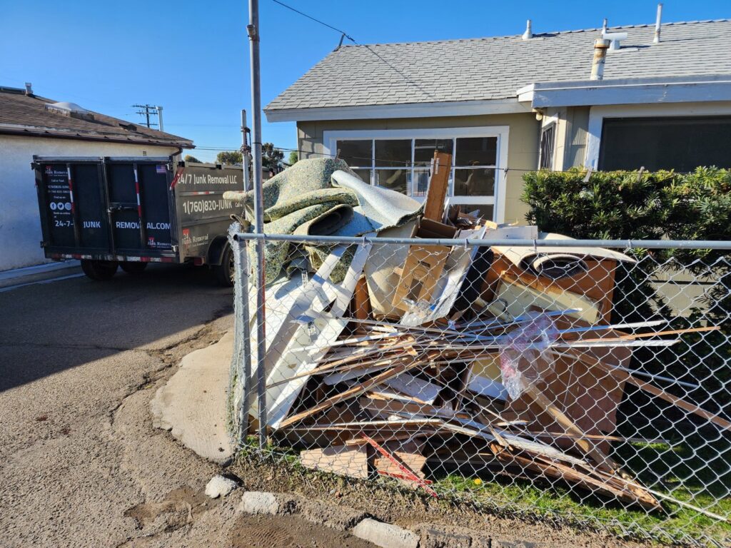 A large pile of construction debris and junk next to a fence, with a 24/7 Junk Removal trailer in Rolling Hills Estates, CA.