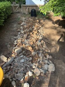 A long pile of construction debris, rocks, and bricks in a backyard for removal by Big John's Demolition & Junk Removal in Charlotte, NC