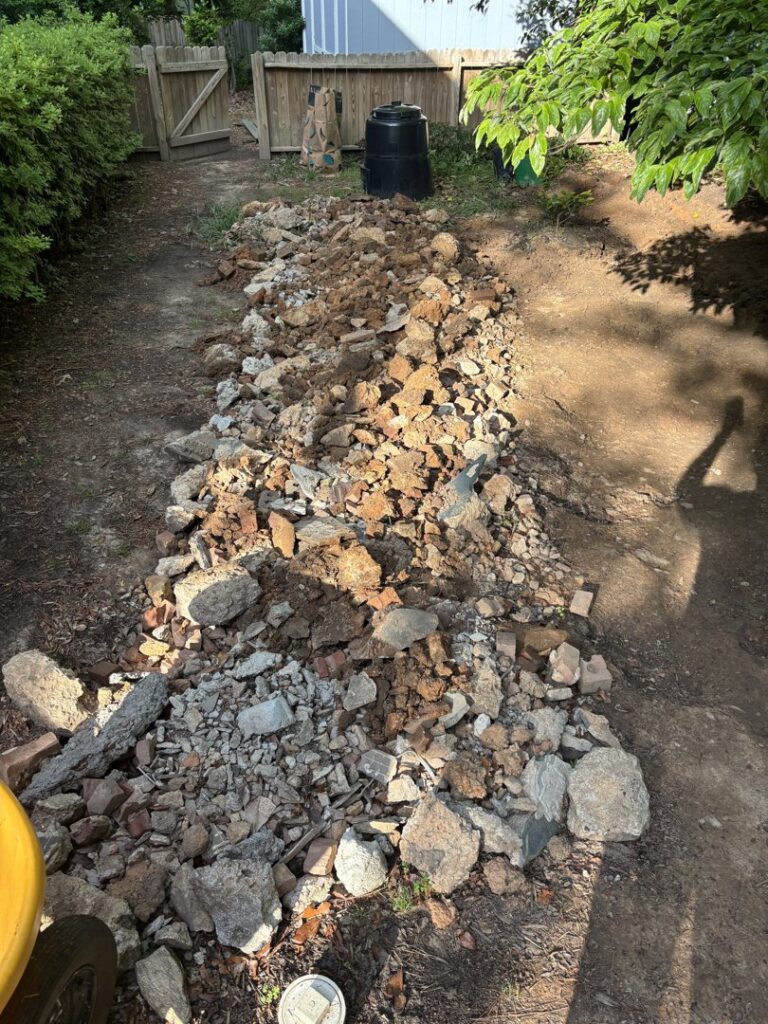 A long pile of construction debris, rocks, and bricks in a backyard for removal by Big John's Demolition & Junk Removal in Charlotte, NC