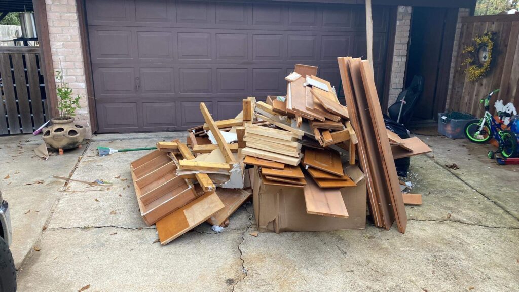 A pile of wood planks and construction debris in front of a garage, ready for general junk removal by Duane's junk removal LLC in Houston, TX.