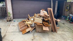 A pile of wood planks and construction debris in front of a garage, ready for general junk removal by Duane's junk removal LLC in Houston, TX.