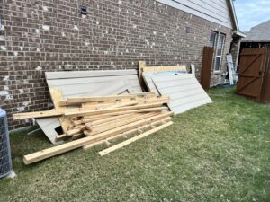 A pile of wooden planks and siding debris next to a house, ready for removal by Hud's Haul Away Junk Removal & Demolition in Fort Worth, TX.