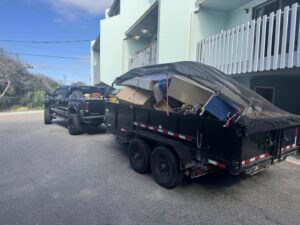 A black pickup truck towing a tarp-covered dump trailer full of junk, ready for transport by Jax Junkies Removal LLC in Jacksonville, FL
