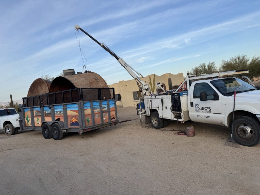 A crane lifting a large metal tank onto a North Valley Junk Removal branded trailer during a heavy junk removal job in Phoenix, AZ.