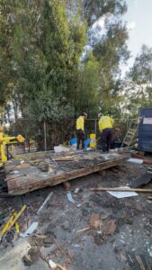 Crisan Junk Removal workers standing on a large pile of wooden debris at a cleanup site in San Diego, CA.