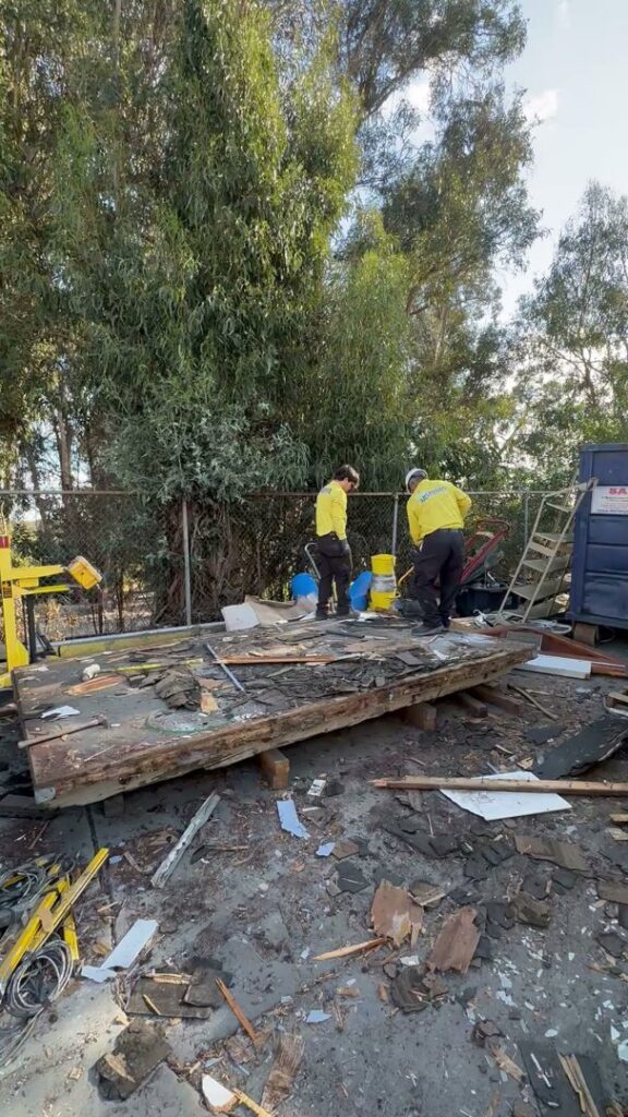 Crisan Junk Removal workers standing on a large pile of wooden debris at a cleanup site in San Diego, CA.