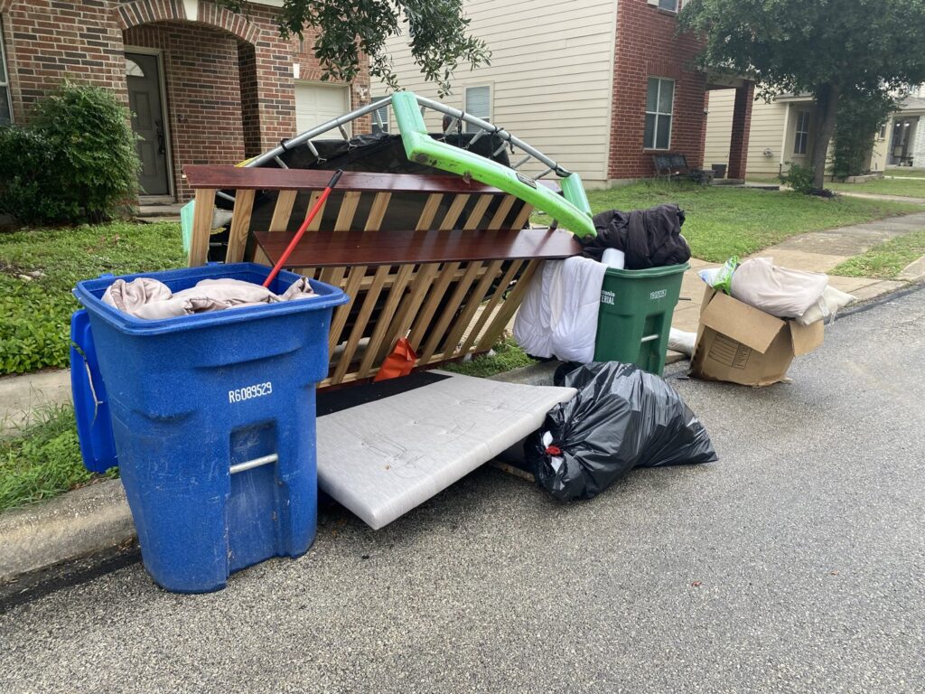 A large pile of household junk, including a mattress and trampoline, placed curbside for removal by Texas Strong Hauling and Junk Removal in San Antonio, TX.