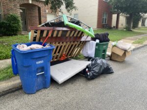 A large pile of household junk, including a mattress and trampoline, placed curbside for removal by Texas Strong Hauling and Junk Removal in San Antonio, TX.
