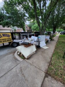 A pile of curbside junk including appliances and debris next to a branded trailer from All Needz Junk Removal & Hauling Service in Dallas, TX.