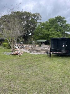 A site with demolition debris and a black roll-off dumpster, showcasing a cleanup job by Jacksonville Hauling & Junk Removal in Jacksonville, FL.