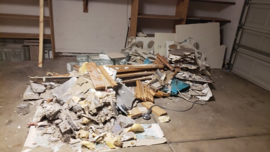 A large pile of demolition debris, including concrete and wood, inside a garage for cleanup by J & R Junk Removal in Phoenix, AZ.