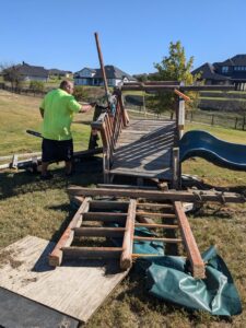 A worker from Herrera Hauling & Junk Removal dismantling a wooden playset with a chainsaw in Fort Worth, TX.