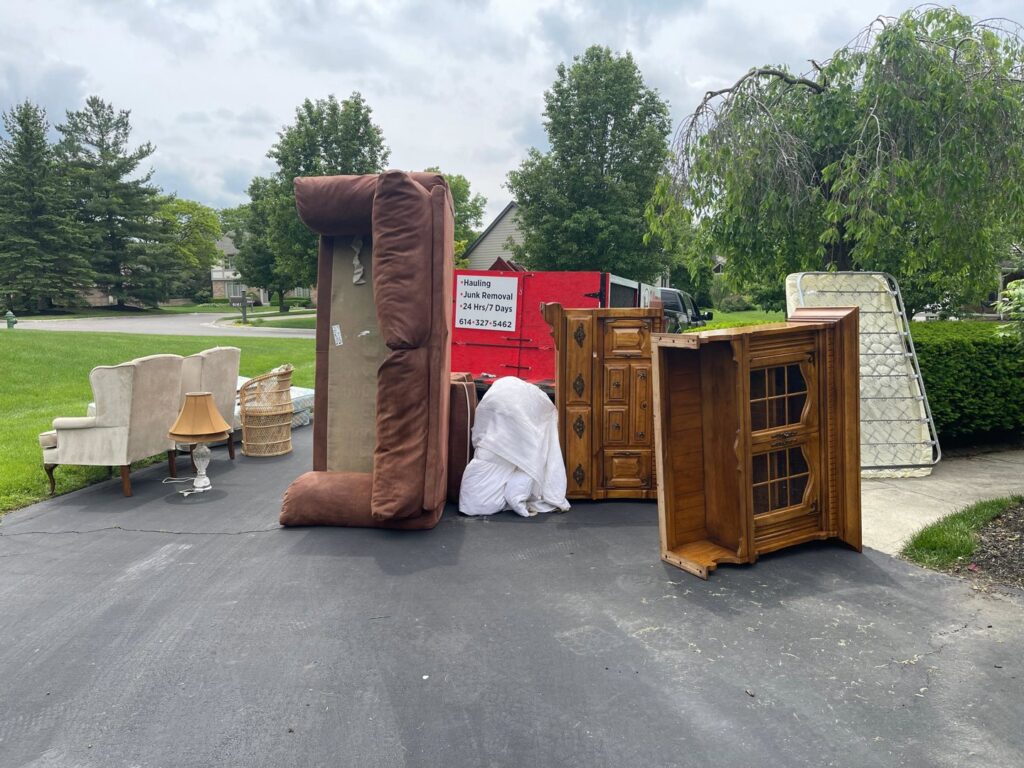 Large furniture items and mattresses piled on a driveway for junk removal by 2 Women with a Pickup Truck and Trailer Too LLC in Columbus, OH.