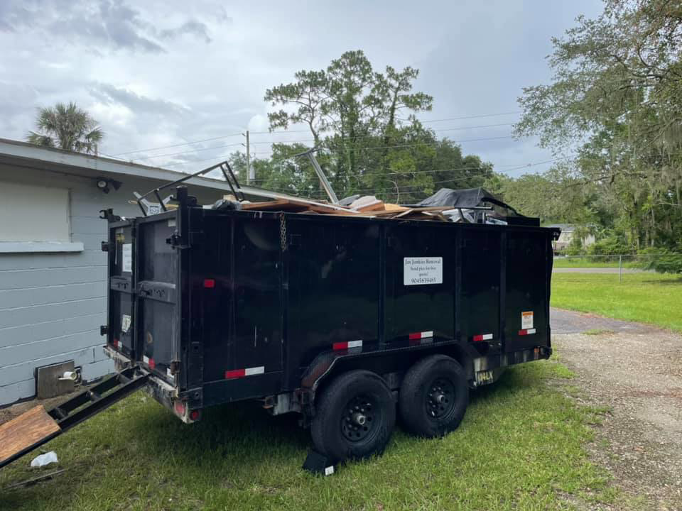 A dump trailer filled with various debris and junk, parked next to a building, handled by Jax Junkies Removal LLC in Jacksonville, FL