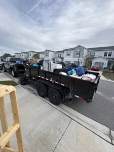 A dump trailer loaded with appliances, boxes, and general junk, towed by a pickup truck for Jax Junkies Removal LLC in Jacksonville, FL