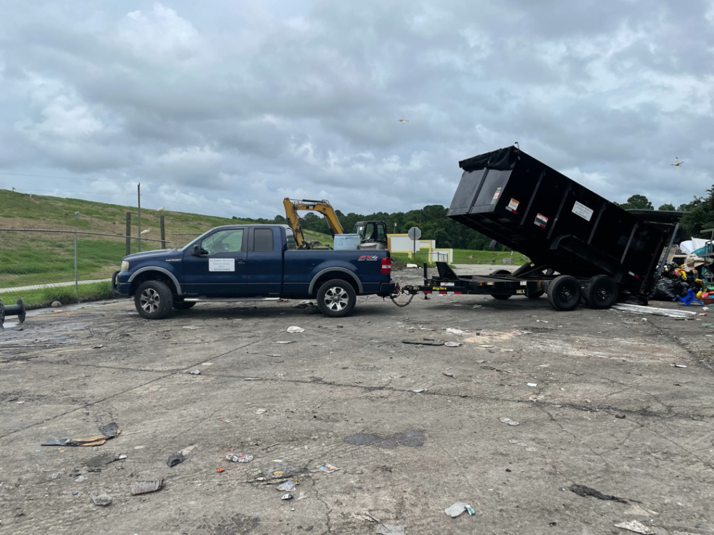 A blue pickup truck with a dump trailer unloading debris at a site, handled by Jax Junkies Removal LLC in Jacksonville, FL