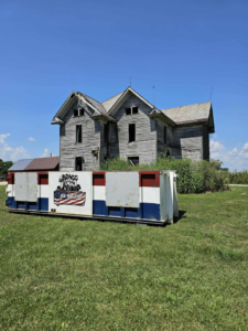 A branded dumpster from Bragg About This Dump placed in front of a dilapidated house in Columbus, OH, ready for junk removal.