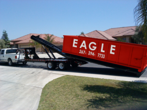 A red Eagle Dumpster Rental dumpster being delivered or picked up by a truck on a residential street in Philadelphia, PA.