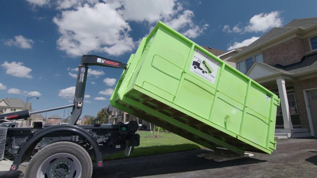 A Bin There Dump That truck delivering a green dumpster to a residential driveway for junk removal in Indianapolis, IN.