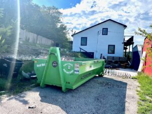 A green 1-800-JUNKPRO dumpster rental placed next to a house with debris, indicating a junk removal job in Austin, TX.