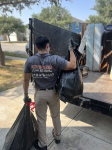A Final Destination Junk Removal employee carrying trash bags to a junk removal trailer in San Antonio, TX.