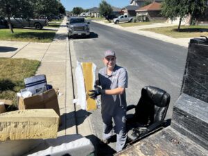 A Final Destination Junk Removal employee loading debris and an office chair into a trailer in San Antonio, TX.