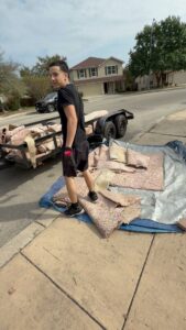 An employee from Faithful Hands Junk Removal in San Antonio, TX, loading old carpet and padding onto a trailer for removal.