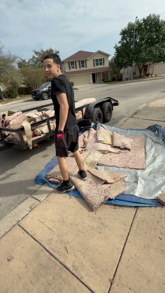 An employee from Faithful Hands Junk Removal in San Antonio, TX, loading old carpet and padding onto a trailer for removal.