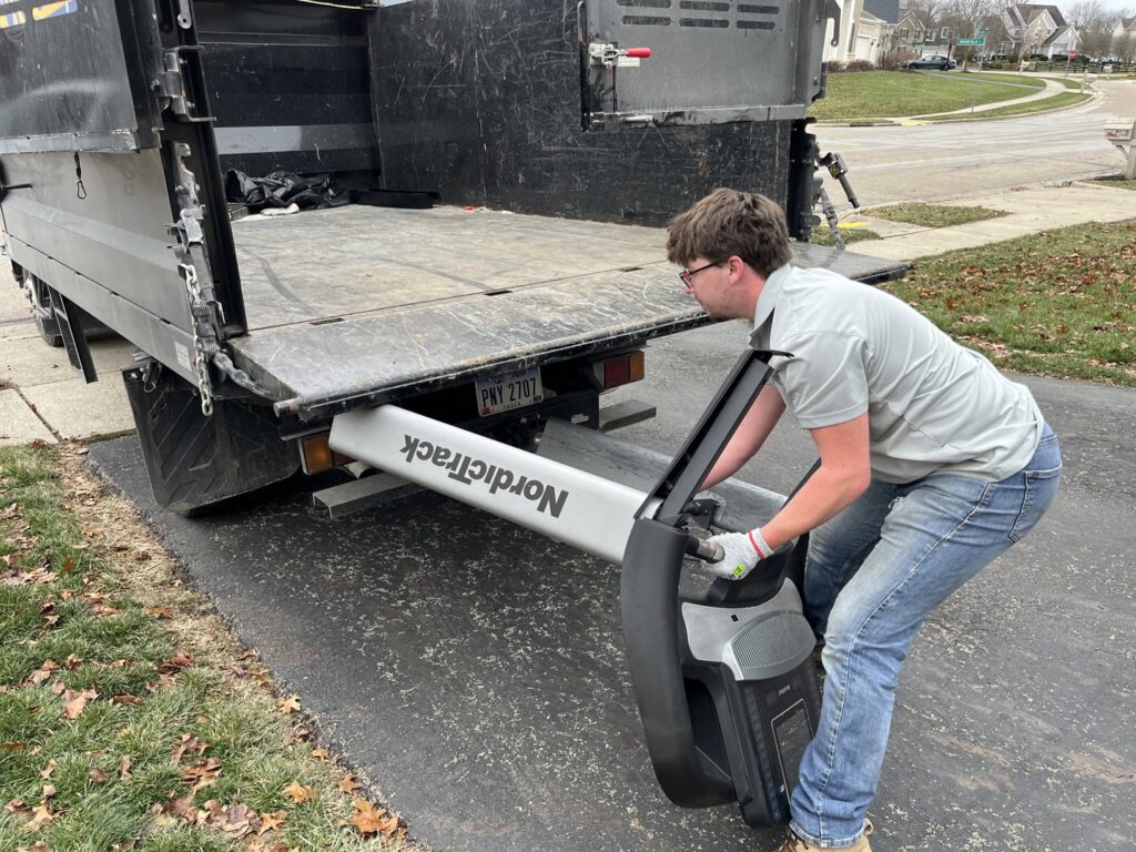 An employee loading a NordicTrack treadmill into a junk removal truck for Lug Stars Junk Removal in Columbus, OH.