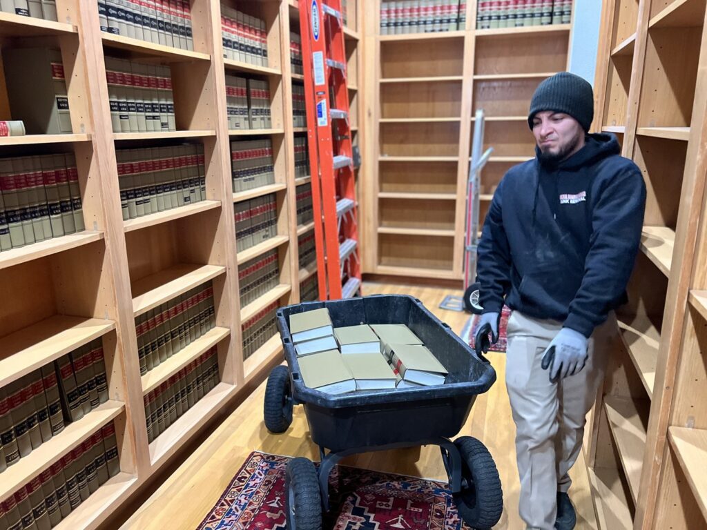 A Final Destination Junk Removal employee using a wheelbarrow to remove books from shelves during a cleanout in San Antonio, TX.