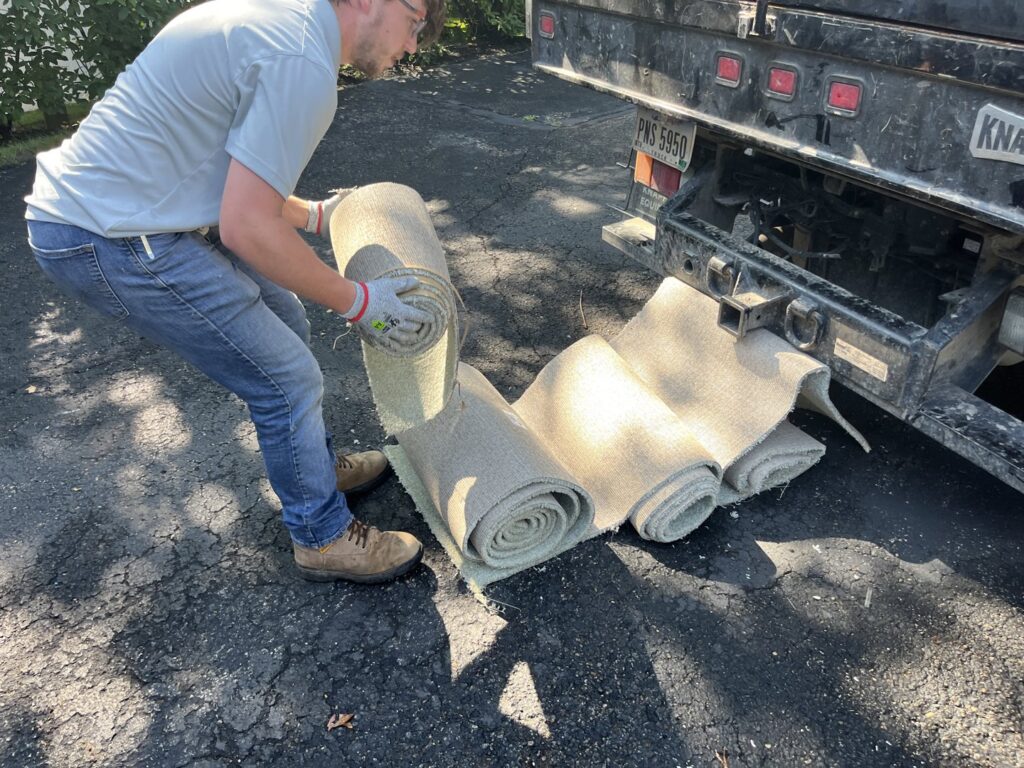 An employee rolling up old carpet for removal by Lug Stars Junk Removal in Columbus, OH.