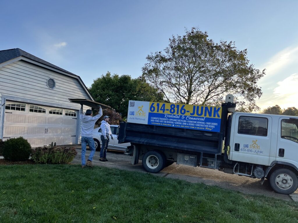 Two employees loading a large flat item into a junk removal truck for Lug Stars Junk Removal in Columbus, OH.